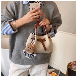 Détail du sac seau en daim crème avec poignées marron et un charmant ours en peluche