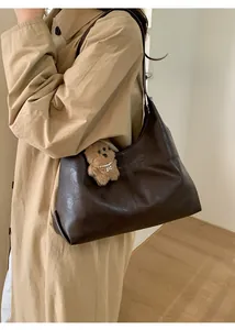 Detail of dark brown leather hobo bag with teddy bear charm shown on shoulder