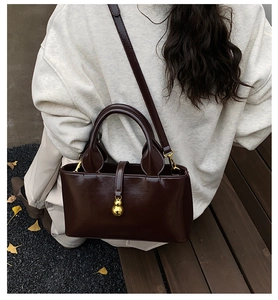 Detail of dark brown glossy leather handbag with a golden gourd pendant on a wooden bench
