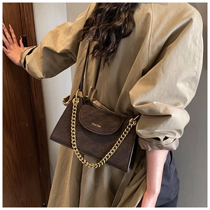 Detail of a deep coffee suede shoulder bag with a gold chain and brand logo on a tan coat