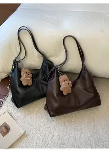 Detail of large black and brown tote bags with cute bear pendants on a soft white rug
