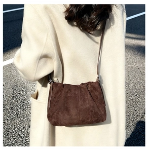 Close-up of pleated dark brown suede bucket bag with silver metal buckle on shoulder strap