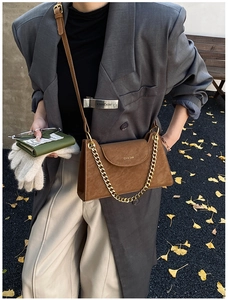 Close-up of brown suede shoulder bag with gold chain strap in an autumn street setting