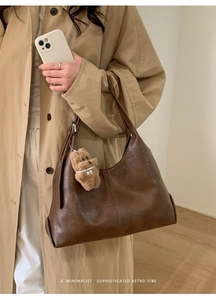 Detail of retro brown crescent tote bag with a soft plush bear charm and leather texture