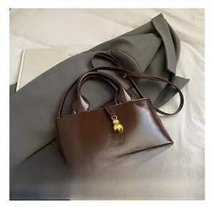 Detail showing deep brown oil wax leather baguette bag with a gold gourd-shaped pendant
