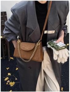 Brown leather crossbody bag with chunky gold chain detail worn by model outdoors