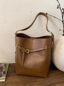 Secchiello minimalista in pelle marrone con finiture dorate su un tavolo di legno