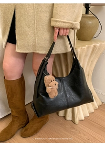 Detail of a black leather tote bag with a vertical stitch and a brown teddy bear charm