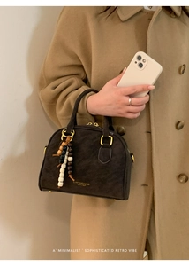 Detail of retro leather handbag with beaded charm, gold hardware and brand logo