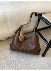 Detail of dark brown leather tote bag with a cute plush bear pendant on a cozy rug