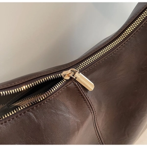 Close-up of golden metal zipper and smooth dark brown leather texture on a shoulder bag