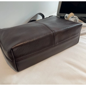 Detail of dark brown leather tote bag with central stitching and laptop on the side