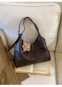 Detail of dark brown leather hobo bag with plush bear charm on white texture sofa