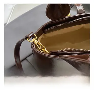 Detail view of gold metal hooks, zipper closure, and beige lining on a brown leather bag