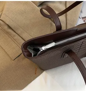 Detail of smooth silver zipper and woven texture on a dark brown tote bag
