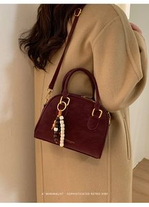 Deep red shell-shaped crossbody bag worn over a camel coat for a vintage commute look