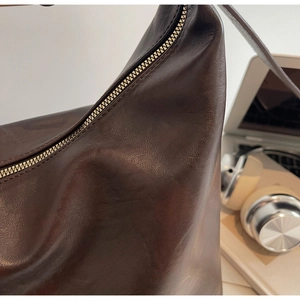 Detail of dark brown leather shoulder bag with glossy texture and metal zipper