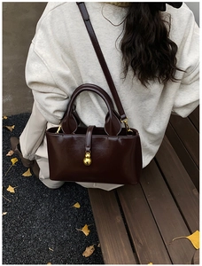 Detailed view of dark brown leather crossbody bag with a gold gourd-shaped pendant charm