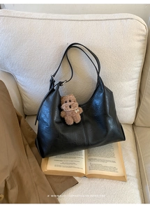 Detail of a black hobo tote bag in textured leather with a cute brown bear pendant charm