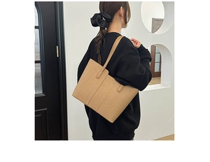 Detailed view of brown herringbone woven tote bag carried by model in a minimalist room