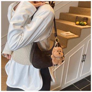 Detail of dark brown crescent underarm bag with gold logo and plush bear charm