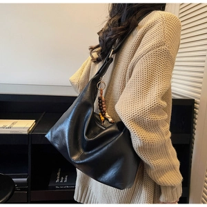 Detail of black leather hobo tote bag featuring ethnic bead charm and silver hardware