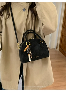 Detail of black suede Boston bag with gold hardware and beaded charm on beige trench coat