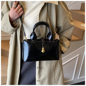 Detail of black patent leather handbag featuring a decorative gold gourd charm