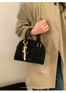 Close-up of black suede semicircular handbag with golden metal handle and beaded pendant