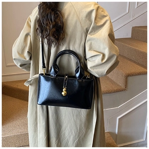 Detail of a black glossy crossbody bag with golden pendant on a model in trench coat