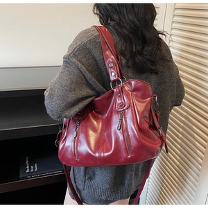Detail view of burgundy leather tote bag with metallic rivets and decorative zippers