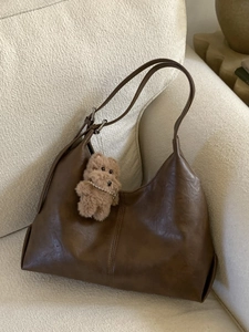 Minimalist brown faux leather tote bag with plush charm on a cozy cream textured sofa