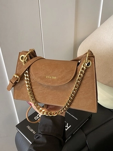 Brown vintage flap shoulder bag with gold chain strap held against a modern background
