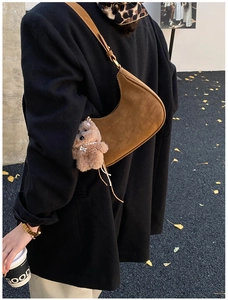 Brown suede underarm bag with cute plush bear charm in a stylish outdoor street setting