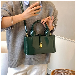 Detail of dark green glossy shoulder bag featuring a unique golden gourd charm attachment