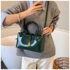 Detail of dark green glossy handbag with gold gourd buckle and crossbody strap
