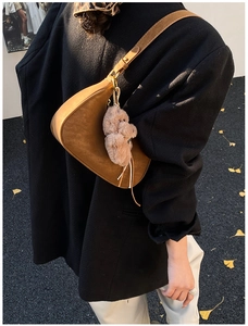 Detail of brown suede crescent shoulder bag with a plush bear charm in autumn outdoor setting