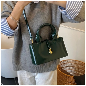 Detail of dark green glossy leather baguette bag with gold gourd charm and strap