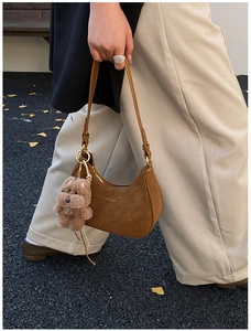Brown suede hobo bag with a plush bear charm and pearl details in a street setting