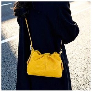 Detail view of yellow pleated cloud bucket bag worn over a dark coat in street style
