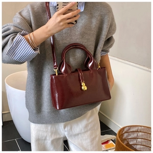 Model wearing a wine red patent leather crossbody bag with metallic ball charm detail