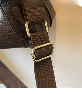 Detail of adjustable shoulder strap connection on dark brown crocodile texture bag