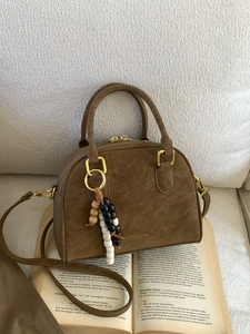 Retro brown suede Boston bag with beaded pendant on a book over white sofa