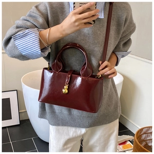 Detail of burgundy patent leather tote featuring a gold gourd-shaped charm and crossbody strap