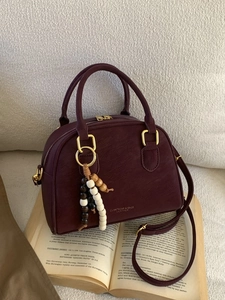 Vintage burgundy leather Boston bag with beaded charm on an open book, warm studio setting