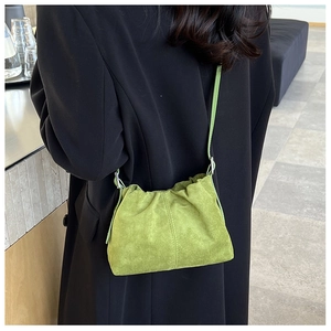 Green suede pleated bucket bag shown as a crossbody on a black blazer jacket
