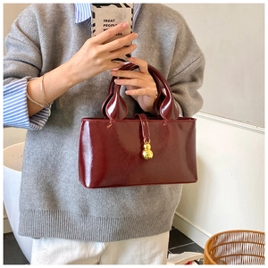 Detail of burgundy red patent leather handbag with gold gourd charm and dual handles