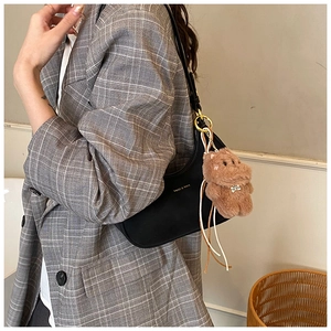Close-up of black half-moon underarm bag with golden logo and brown plush bear charm