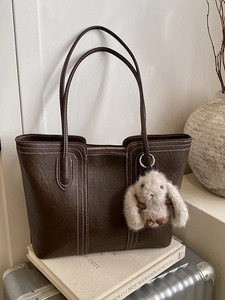 Braune Shopper-Tasche mit Kontrastnaht und Hasen-Anhänger auf silbernem Koffer