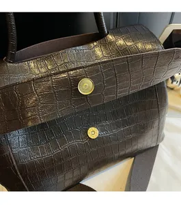 Detail of the magnetic snap closure on a dark brown crocodile embossed tote bag